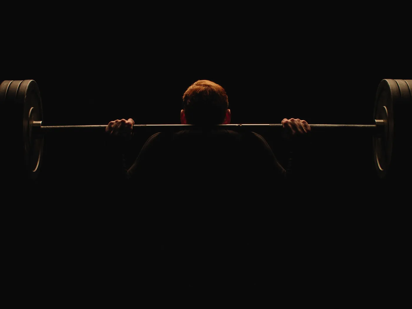 Atleta de espalda levantando una barra en un gimnasio oscuro