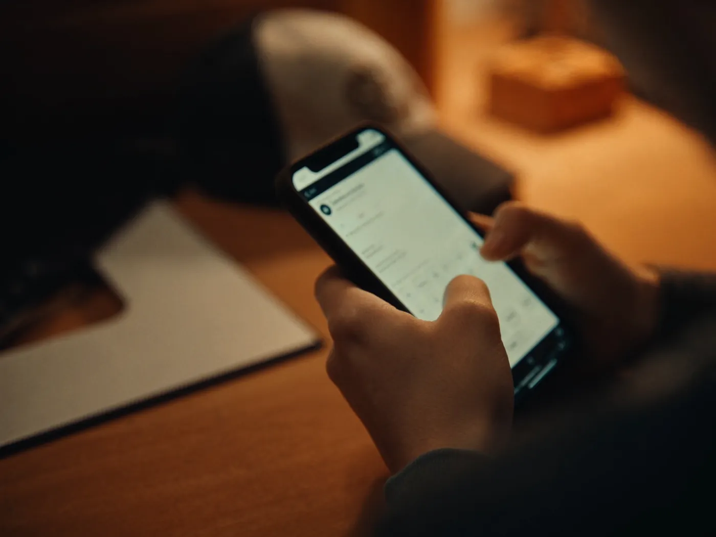 Manos escribiendo en un teléfono sobre una barra de cocina, de noche